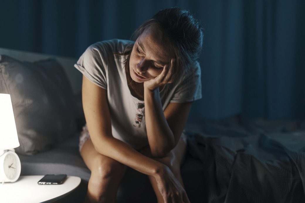 Donna sveglia di notte sul bordo del letto, accanto una sveglia