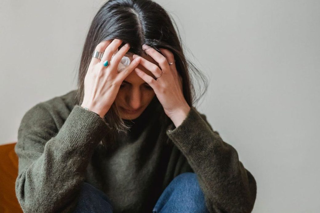 Frau sitzt zusammengesunken, die Hände im Haar